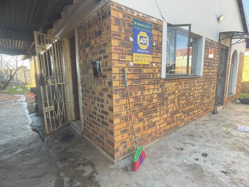 Rear exterior view of the house featuring face brick walls, a paved patio area, and security installations.