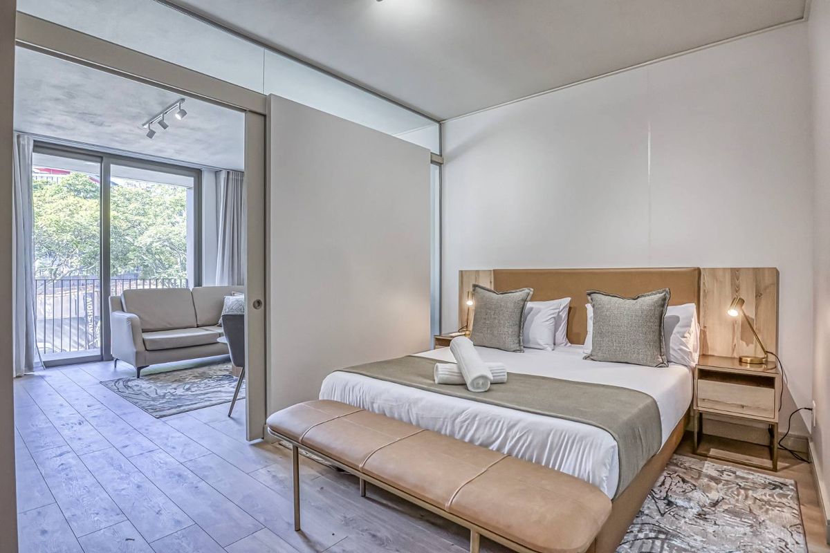 Modern bedroom featuring a sliding glass partition wall, light wood-look flooring, and direct access to a private balcony.