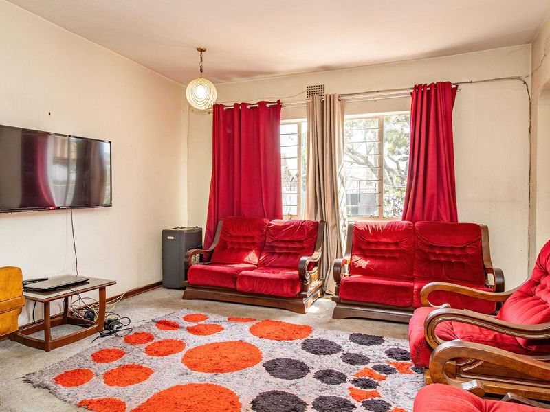 A dated living room featuring steel-framed windows and carpet flooring, offering a blank canvas for modernization and interior design updates.