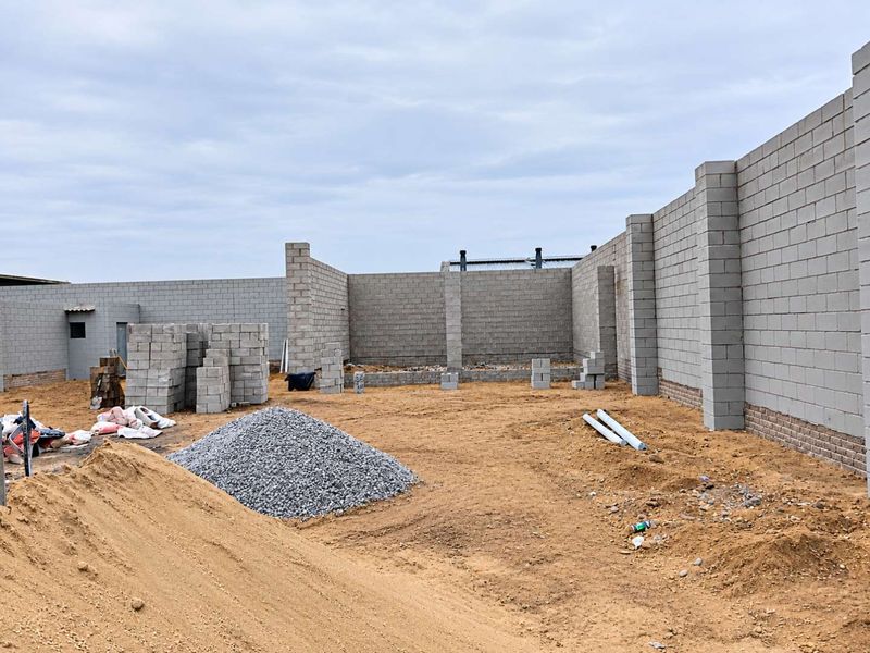An industrial property under construction featuring exposed concrete block perimeter walls and structural pillars on an unpaved site.