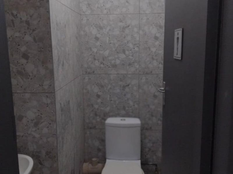 A compact bathroom featuring modern grey terrazzo-style wall tiles, a white toilet, and a small basin.