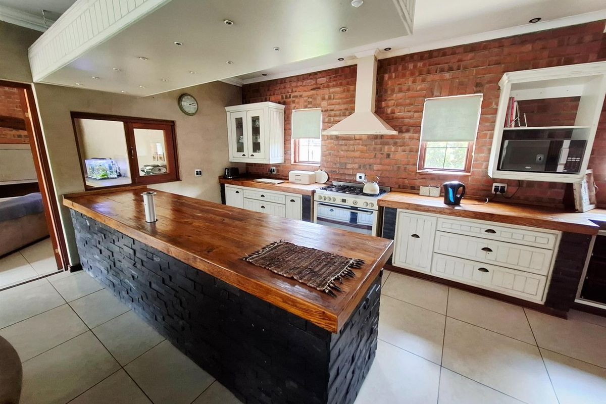 Spacious kitchen featuring exposed brick walls, a large central island with a wooden countertop, gas stove, and ample built-in cabinetry.