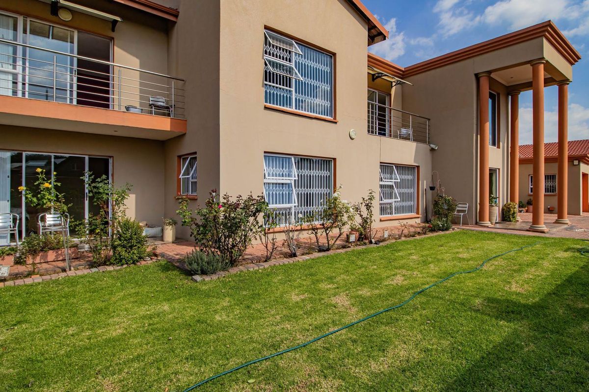 Rear view of a two-story residential property featuring a landscaped garden, paved patio area, upper-level balconies, and classic architectural columns.