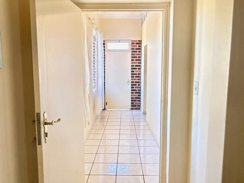 A bright, tiled hallway leading to an exterior entrance door, featuring clean lines and neutral wall finishes.