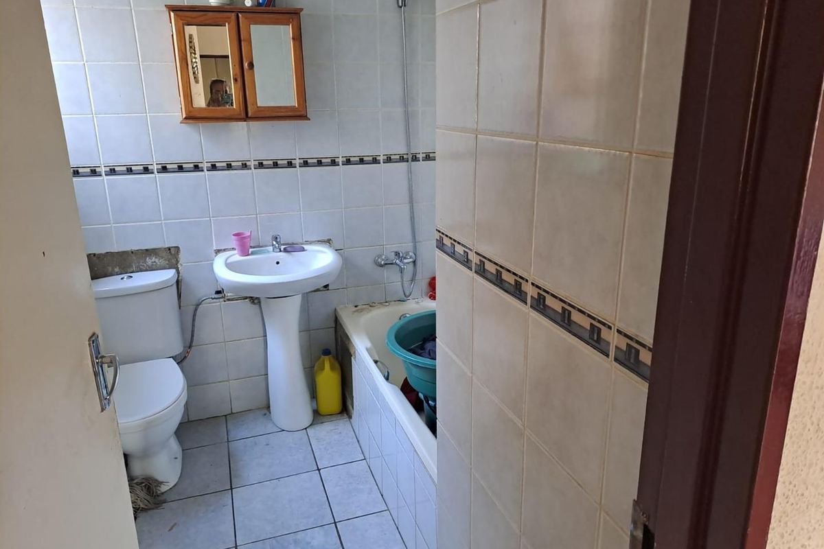 A dated bathroom featuring a pedestal sink, standard toilet, and a bathtub with a shower mixer, requiring cosmetic updates and tile repairs.
