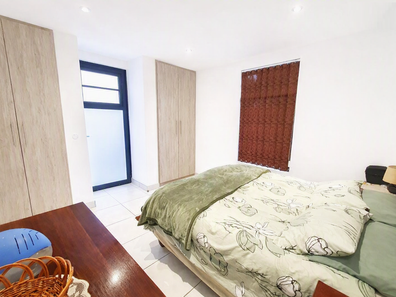A bright bedroom featuring tiled flooring, recessed downlights, and ample built-in cupboard storage with direct access to an exterior area.