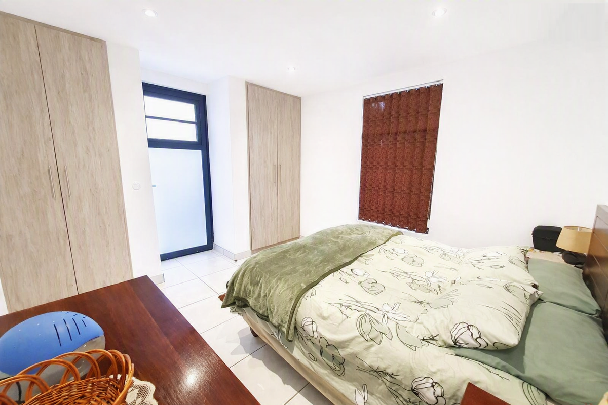 A bright bedroom featuring tiled flooring, recessed downlights, and ample built-in cupboard storage with direct access to an exterior area.
