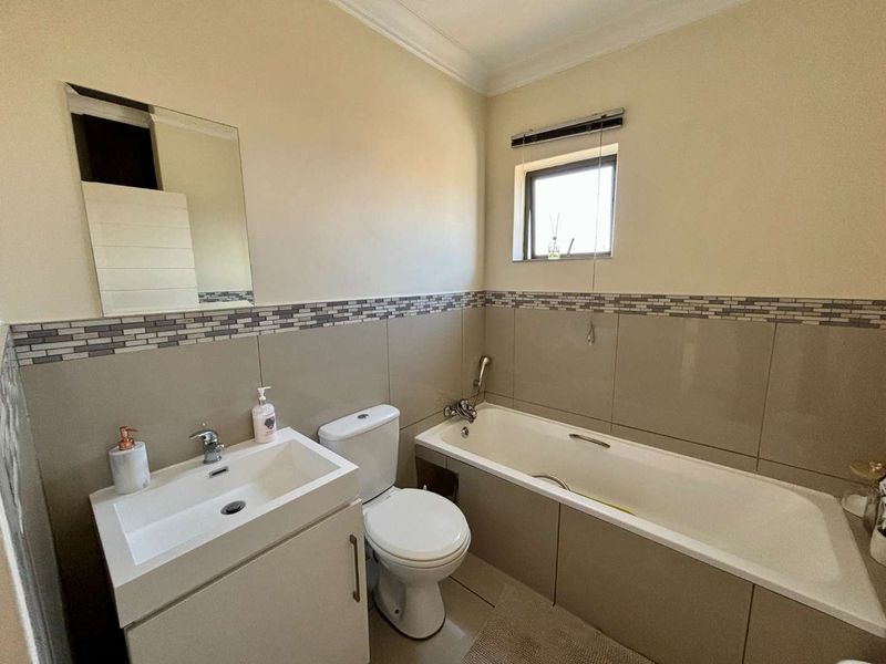 A functional bathroom featuring a vanity basin, toilet, and bathtub with neutral wall tiling and a decorative mosaic border.