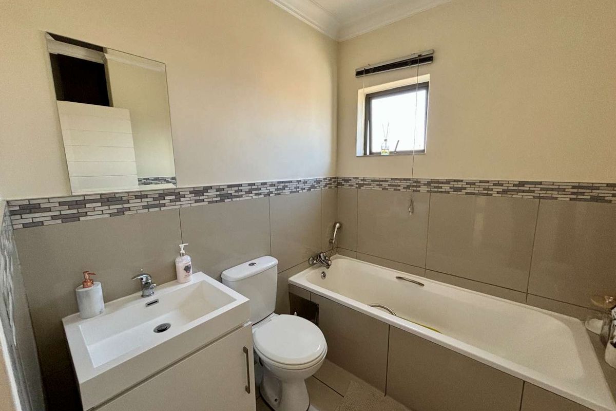 A functional bathroom featuring a vanity basin, toilet, and bathtub with neutral wall tiling and a decorative mosaic border.