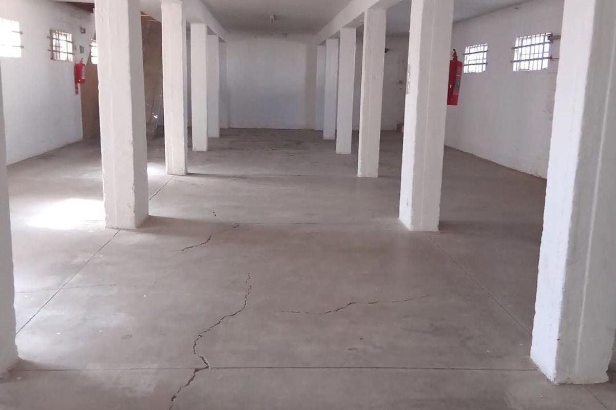 An expansive, open-plan industrial utility space featuring concrete flooring, structural support columns, and security-barred windows, suitable for storage or workshop use.