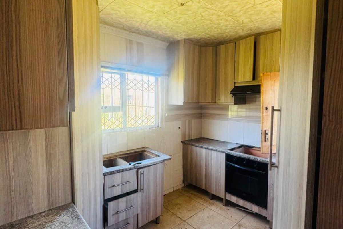 A dated kitchen featuring wood-look cabinetry, tiled flooring, and a window with security bars, currently requiring significant maintenance and fixture replacement.