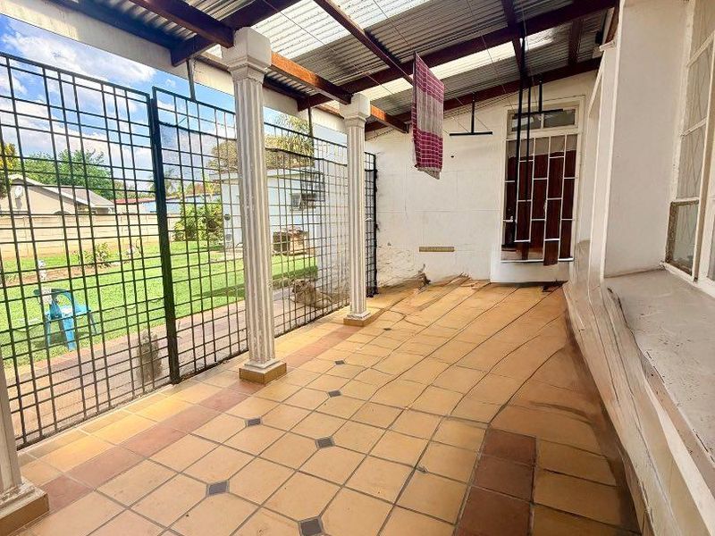 A covered outdoor patio area featuring tiled flooring, decorative columns, and a corrugated roof, offering a functional space for outdoor living.