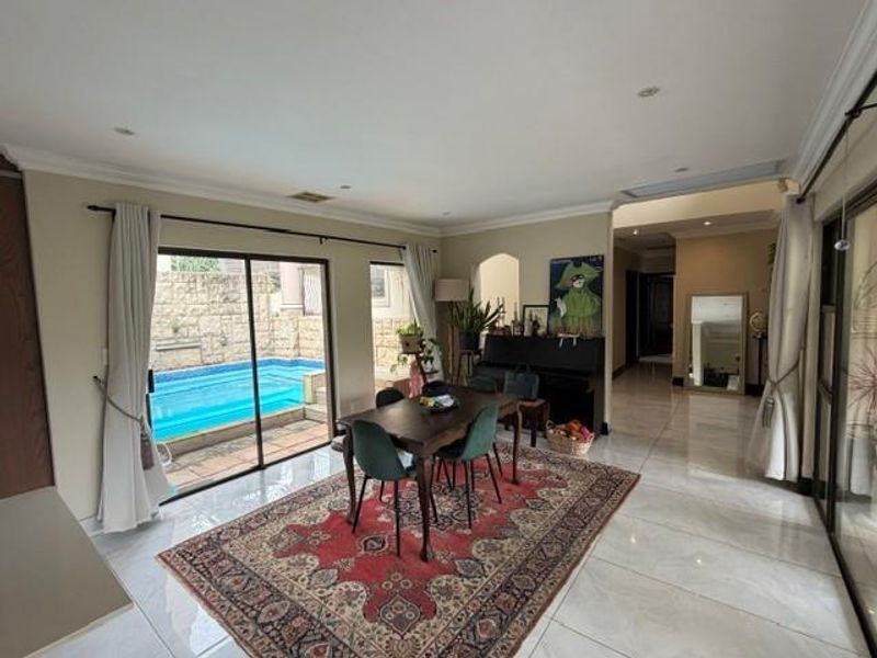 Dining area featuring large sliding glass doors that open to a private pool area, complemented by polished tiled flooring and recessed lighting.