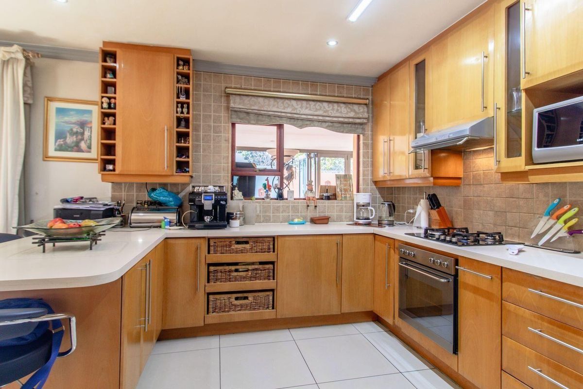 A functional kitchen featuring light wood cabinetry, tiled backsplash, built-in oven, gas hob, and an integrated extractor fan with white tiled flooring.