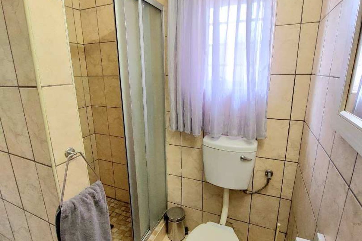 A compact bathroom featuring a tiled shower enclosure, a standard toilet, and neutral wall and floor tiling.
