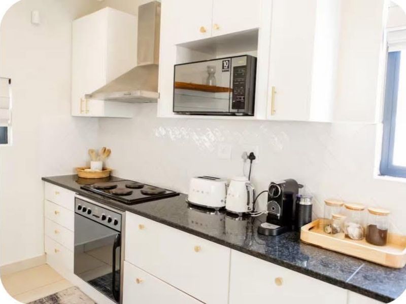 Modern kitchen featuring white cabinetry, granite countertops, a built-in oven, electric hob, and a stainless steel extractor fan.