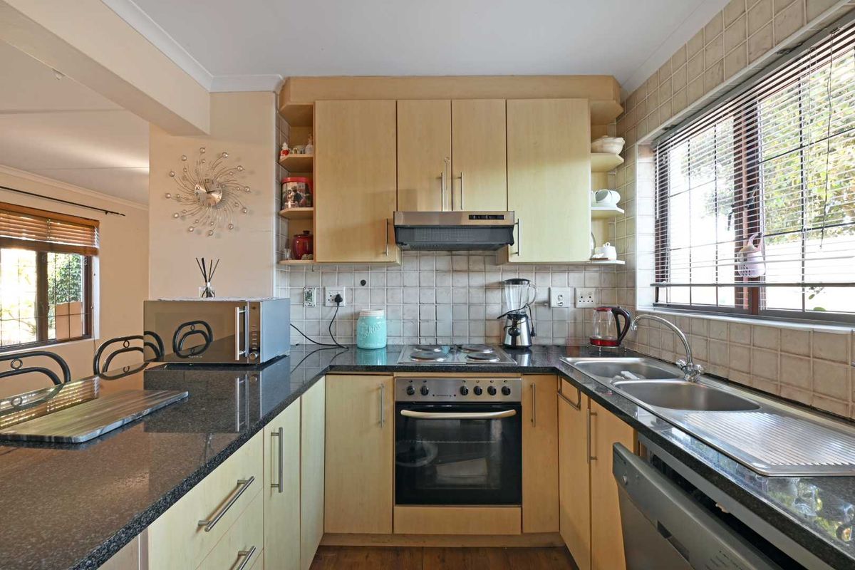 A functional kitchen featuring light wood cabinetry, granite countertops, a built-in oven with hob, and a double stainless steel sink with tiled backsplash.