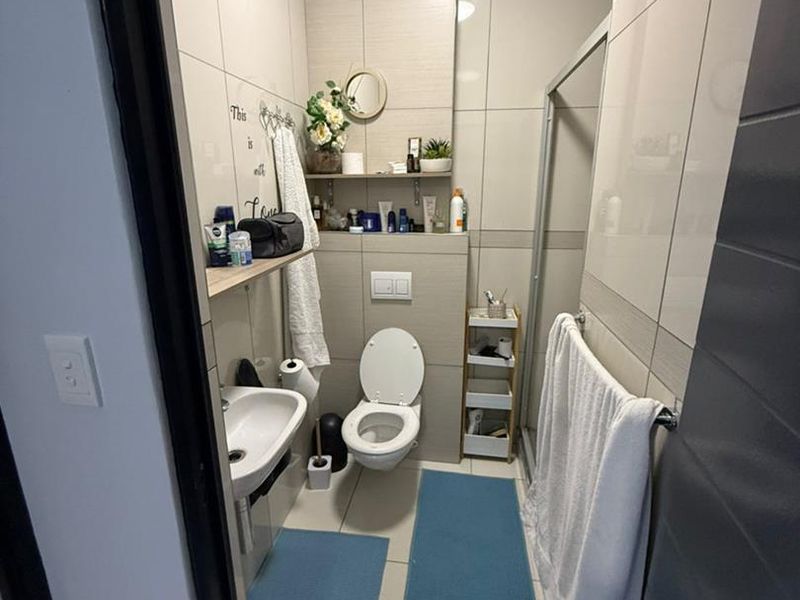 A compact bathroom featuring floor-to-ceiling ceramic tiling, a wall-mounted toilet, and a glass-enclosed shower area.