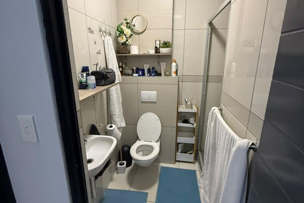 A compact bathroom featuring floor-to-ceiling ceramic tiling, a wall-mounted toilet, and a glass-enclosed shower area.