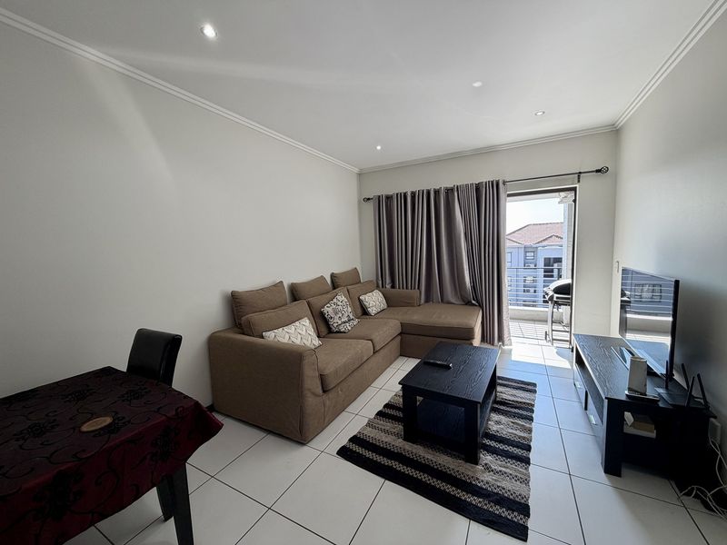 A bright, open-plan living area featuring tiled floors, recessed lighting, and direct access to a private balcony through a sliding glass door.