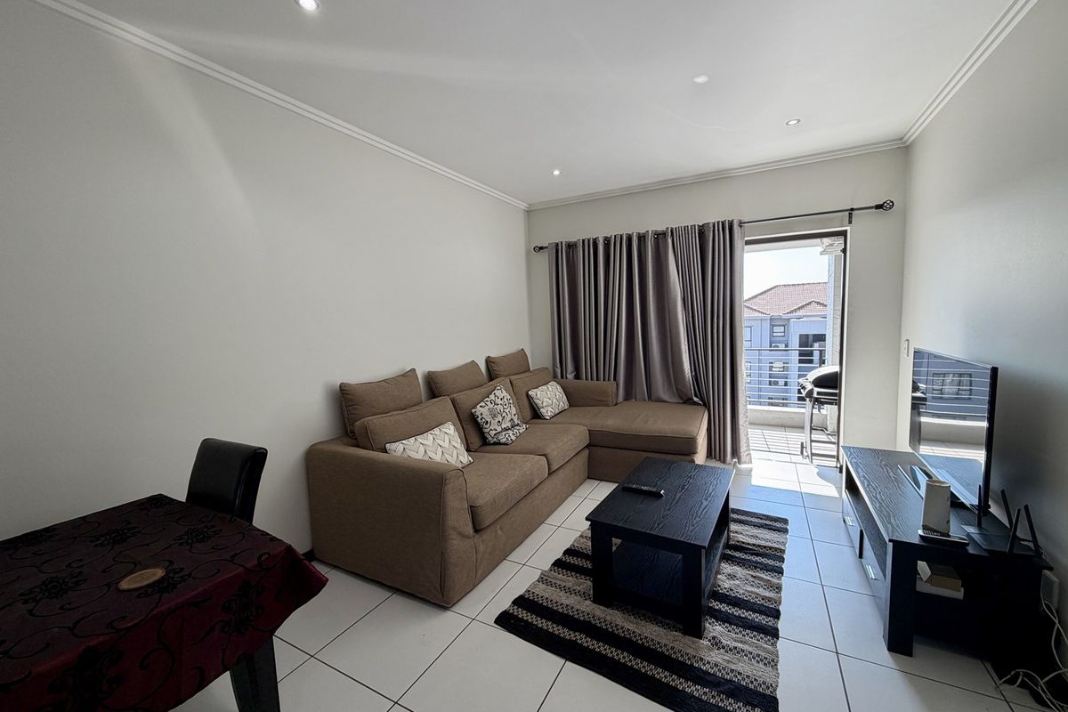 A bright, open-plan living area featuring tiled floors, recessed lighting, and direct access to a private balcony through a sliding glass door.