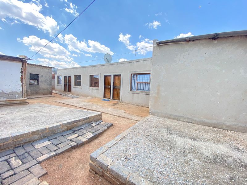 Rear exterior view of the residential property featuring multiple access points, security gates, and paved outdoor areas with concrete platforms.