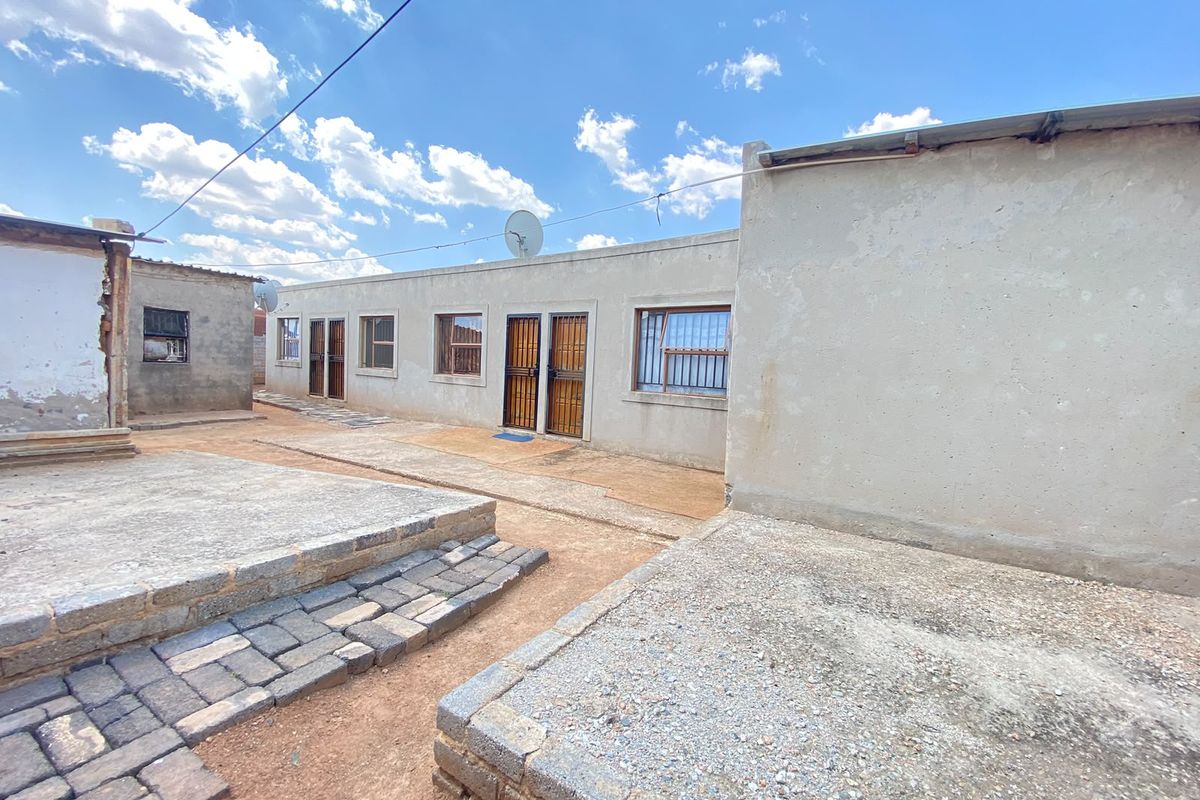 Rear exterior view of the residential property featuring multiple access points, security gates, and paved outdoor areas with concrete platforms.