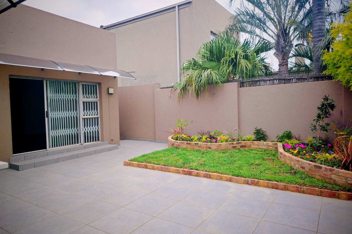 A well-maintained rear courtyard featuring tiled patio flooring, a manicured lawn with a brick-edged garden bed, and secure sliding glass doors with security gates.