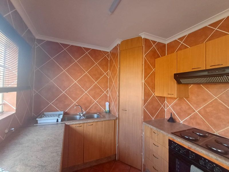 A functional kitchen featuring wood-look cabinetry, laminate countertops, a built-in oven with extractor fan, and distinctive diagonal wall tiling.