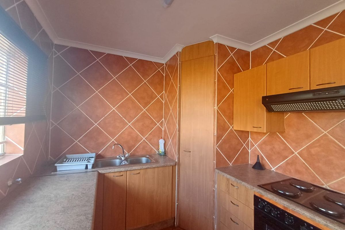 A functional kitchen featuring wood-look cabinetry, laminate countertops, a built-in oven with extractor fan, and distinctive diagonal wall tiling.