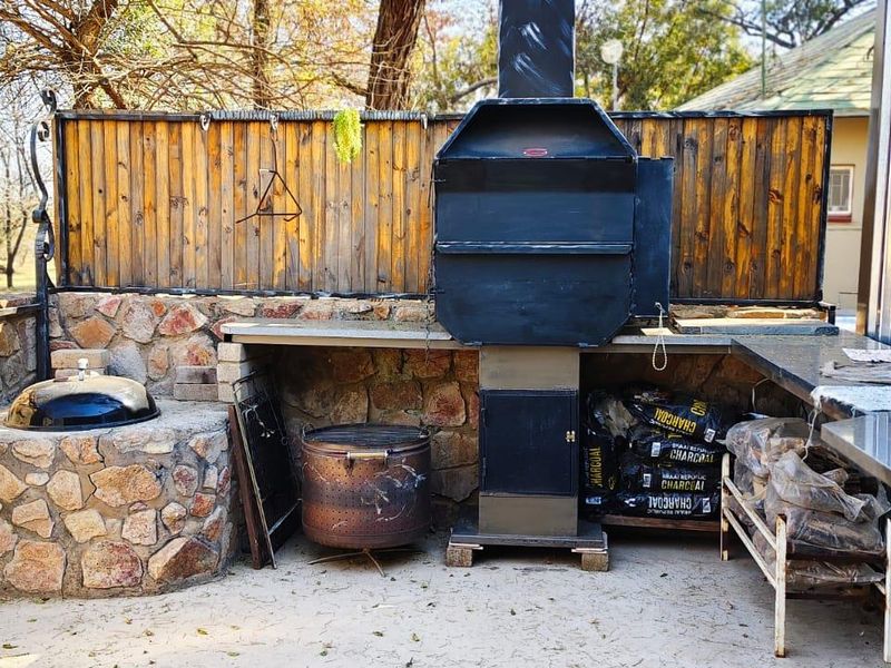 Outdoor entertainment area featuring a built-in braai, stone-clad prep surfaces, and a sink, set against a rustic timber fence.