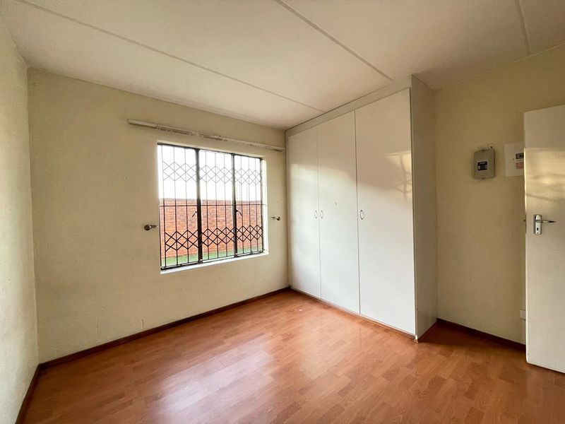 An empty bedroom featuring laminate flooring, built-in cupboards, and a window fitted with security bars.