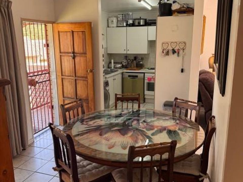 Open plan dining area adjacent to a functional kitchen with built-in cabinetry and tiled flooring, featuring direct access to an exterior security gate.