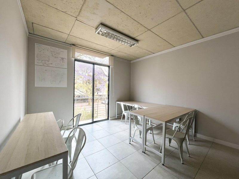 A functional office space featuring tiled flooring, a sliding glass door providing natural light, and a suspended ceiling with integrated lighting.