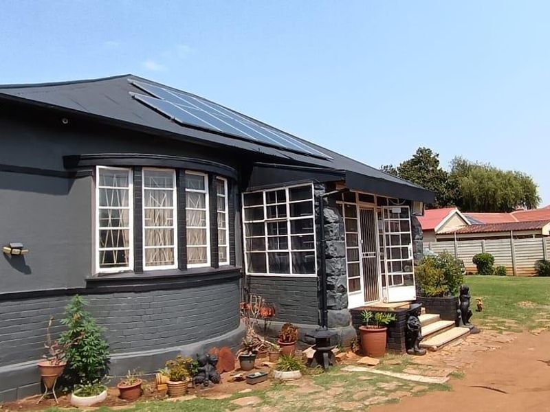 Rear view of a dark-painted brick house featuring a metal roof with installed solar panels and a small garden area.