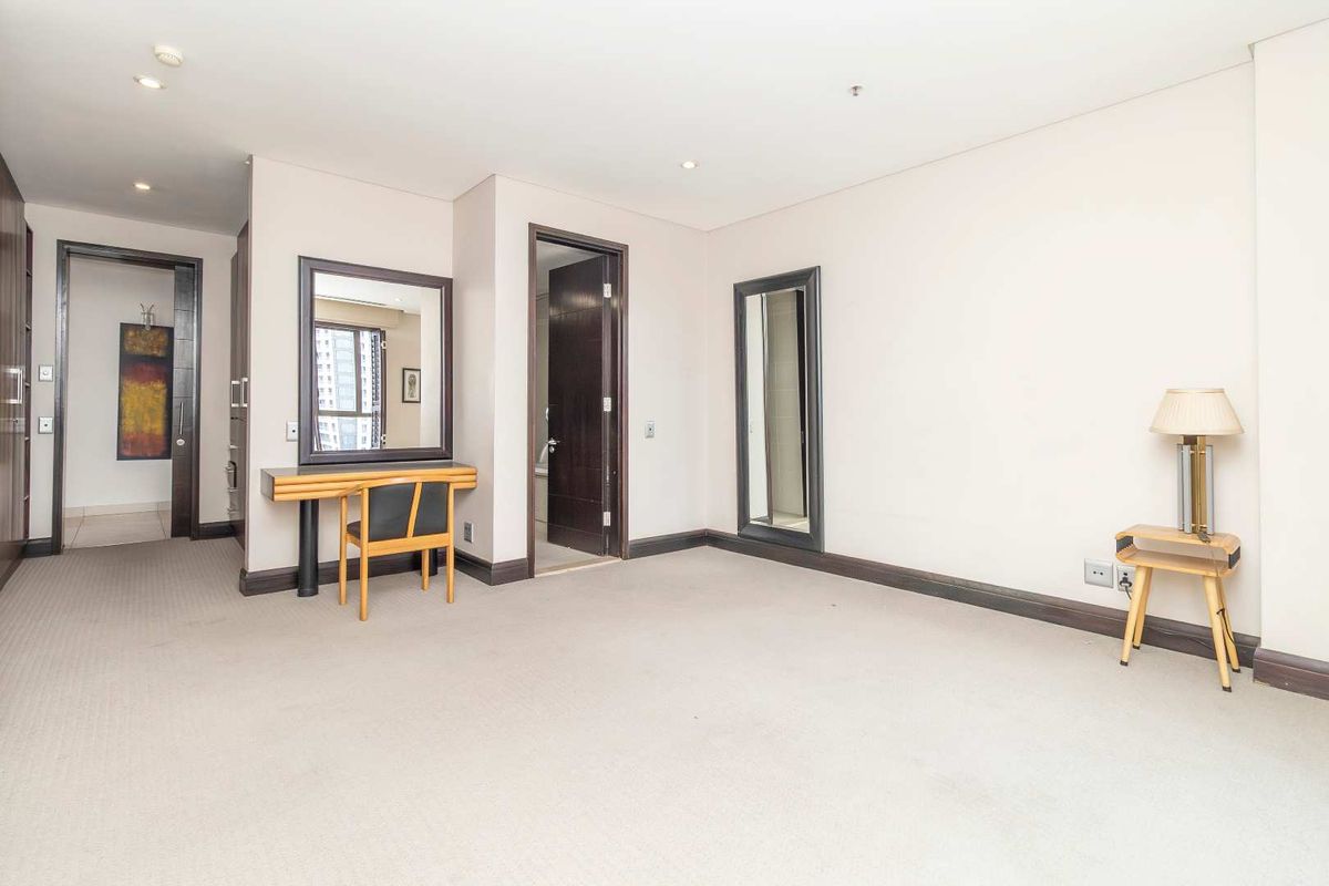 Spacious bedroom featuring neutral carpeting, recessed ceiling lighting, dark wood door frames, and a built-in vanity area with an integrated mirror.