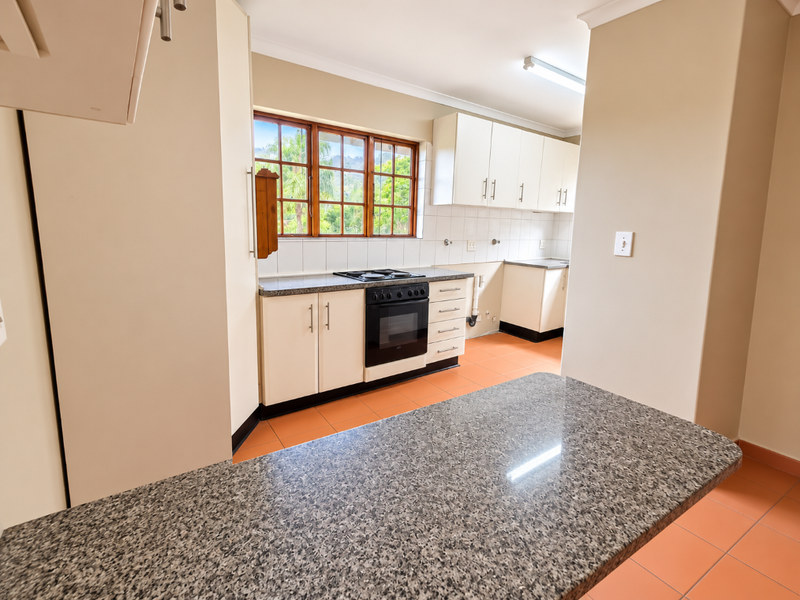 A functional kitchen featuring built-in cabinetry, granite countertops, a built-in oven with hob, and tiled flooring, offering a clean and practical workspace.