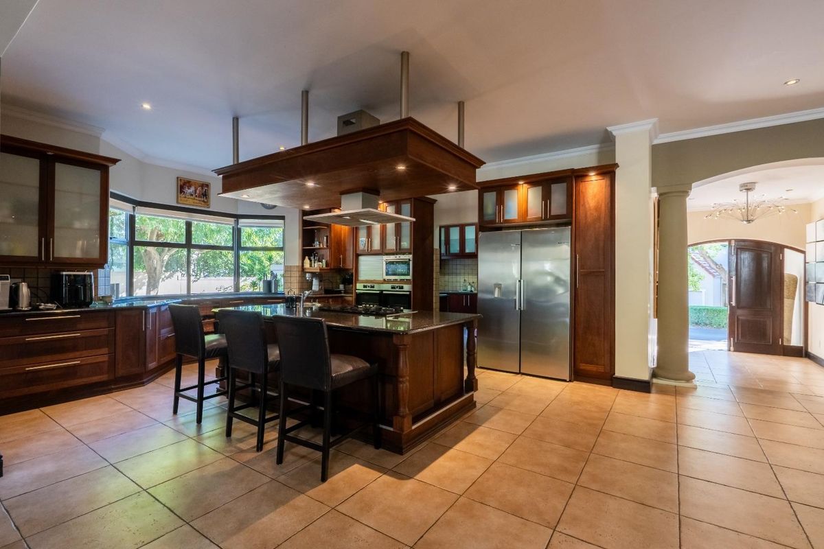 Spacious kitchen featuring dark wood cabinetry, a central island with a built-in cooktop, granite countertops, and a large stainless steel double-door refrigerator.