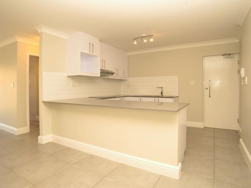 A clean, modern kitchen featuring white cabinetry, stone countertops, subway tile backsplash, and tiled flooring, presented in an empty, well-maintained state.