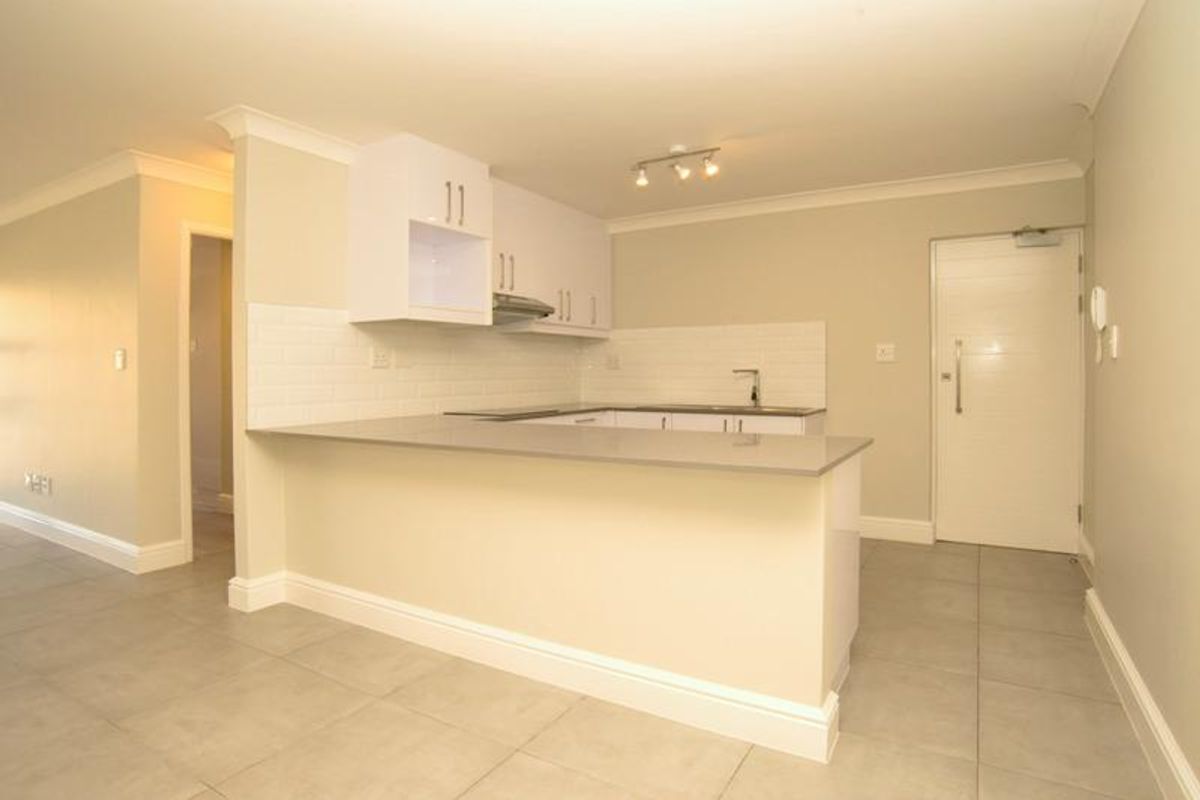 A clean, modern kitchen featuring white cabinetry, stone countertops, subway tile backsplash, and tiled flooring, presented in an empty, well-maintained state.