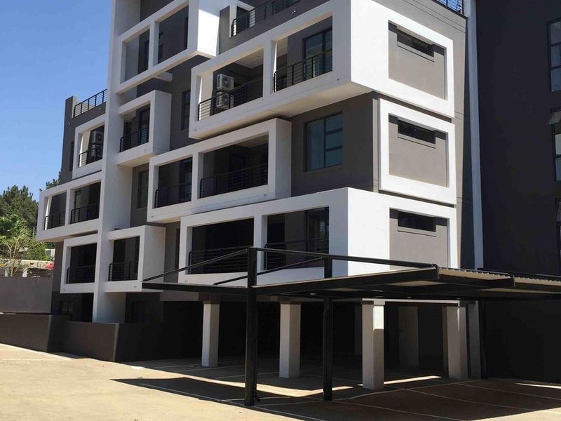 Modern multi-story apartment building featuring contemporary architectural design, private balconies, and a covered carport area.