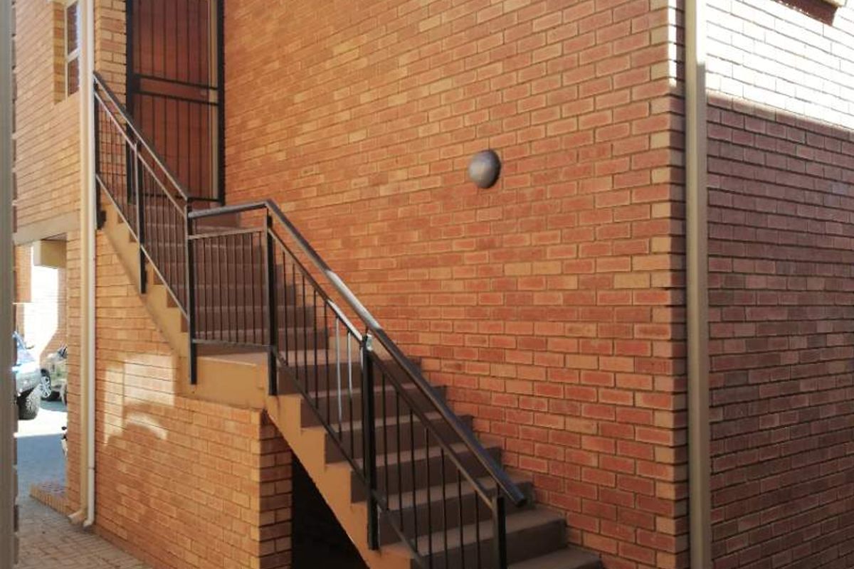 Exterior view of an apartment building featuring a brick facade, external staircase with metal railing, and paved ground area.