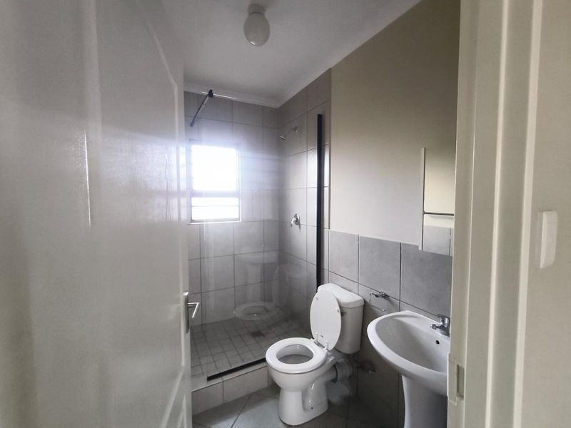 A clean and functional bathroom featuring a walk-in shower with a glass screen, a pedestal basin, and neutral wall and floor tiling.