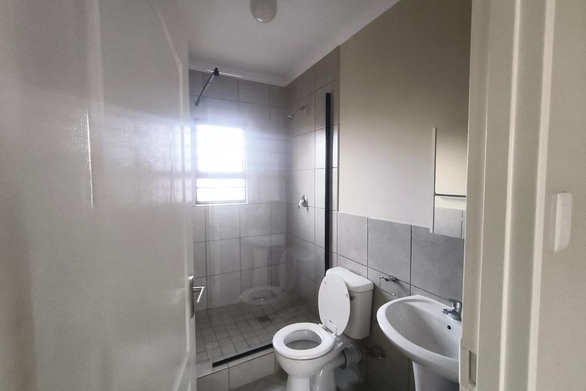 A clean and functional bathroom featuring a walk-in shower with a glass screen, a pedestal basin, and neutral wall and floor tiling.
