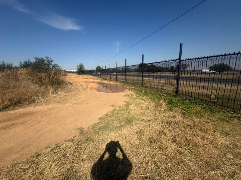 An exterior view of the property boundary featuring security fencing along an unpaved access road with visible ground surface irregularities.