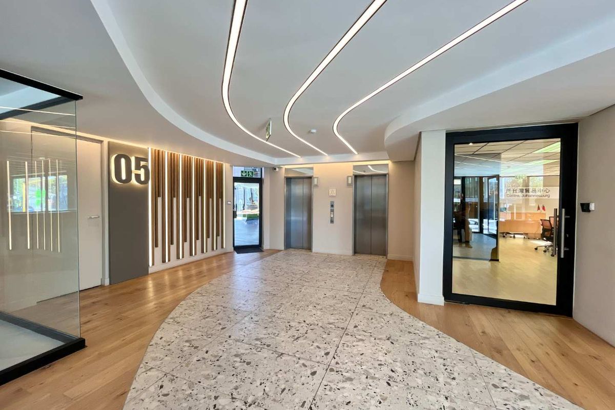 Modern office building lobby featuring high-end finishes, including a combination of terrazzo and hardwood flooring, recessed linear ceiling lights, and stainless steel elevator access.