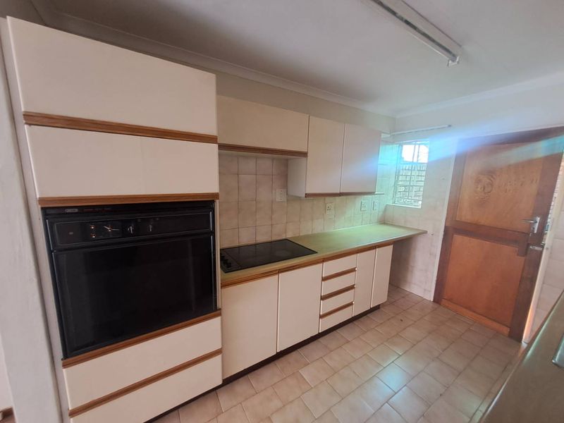A functional kitchen featuring built-in cabinetry, a wall-mounted oven, and a cooktop, with tiled flooring and a rear access door.