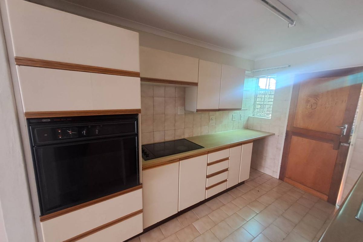 A functional kitchen featuring built-in cabinetry, a wall-mounted oven, and a cooktop, with tiled flooring and a rear access door.