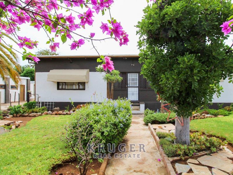 Front view of a residential house featuring a landscaped garden, paved walkway, and a security gate entrance.