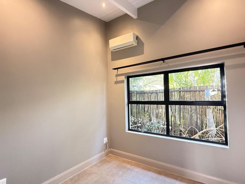 A bright, empty bedroom featuring tiled flooring, a modern black-framed window, and a wall-mounted air conditioning unit.
